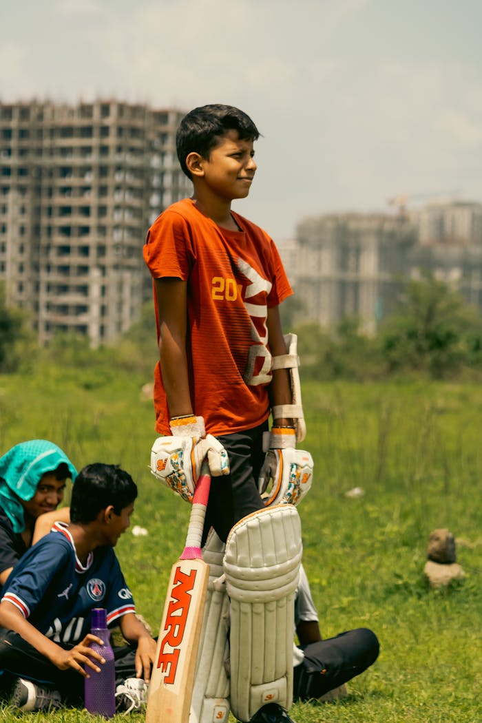 services-04 Children enjoying a cricket game outdoors near city buildings.