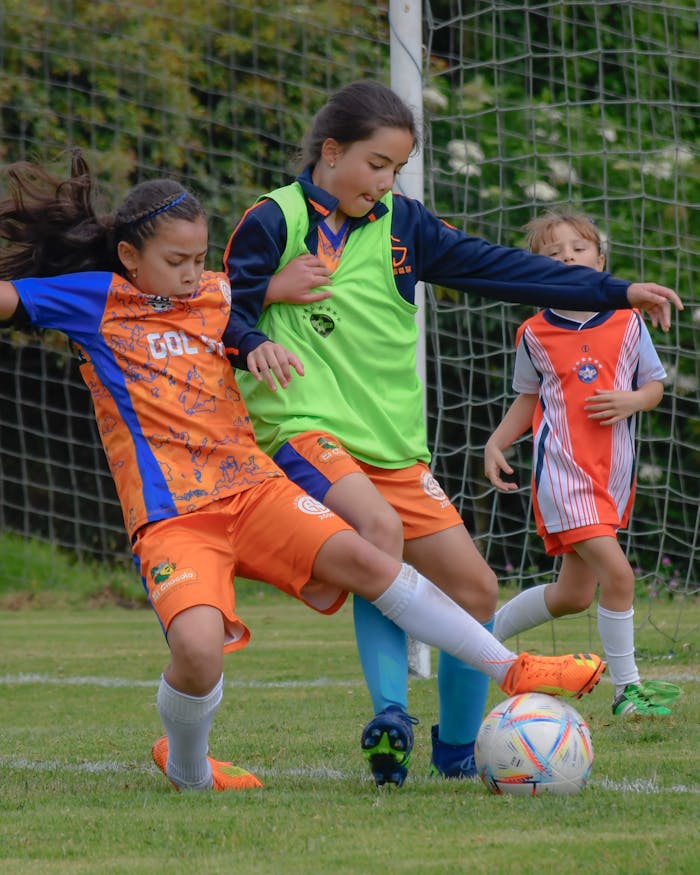 about-img Three young girls actively playing a soccer match outdoors, showcasing team spirit and sportsmanship.