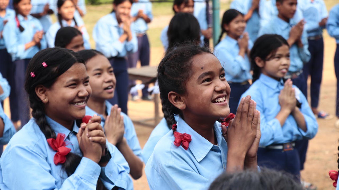 ours-journey Cheerful schoolgirls in uniforms smiling outdoors during a school event.