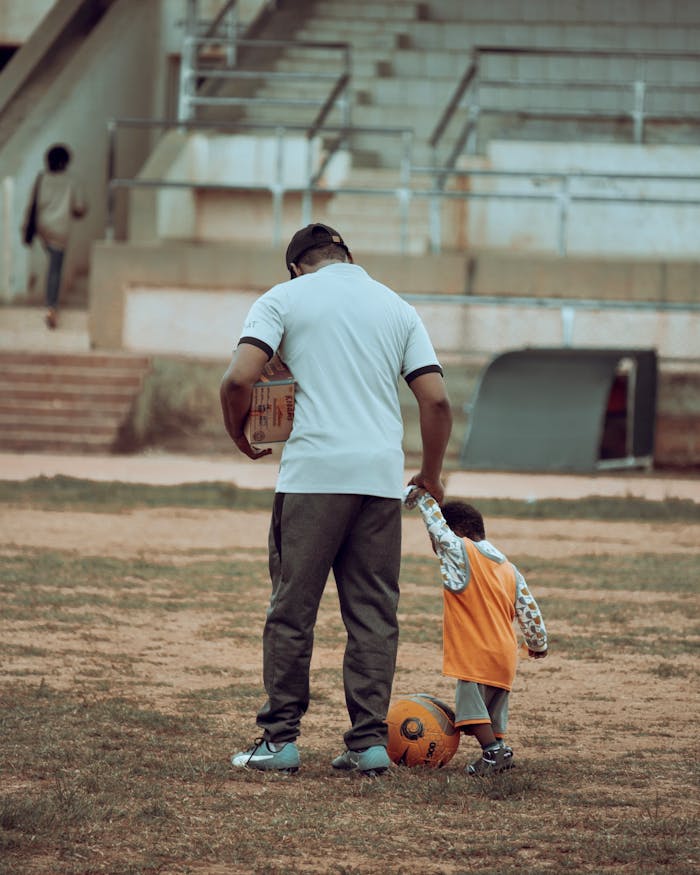 our-experience A father and child bonding over a soccer ball on an outdoor field.