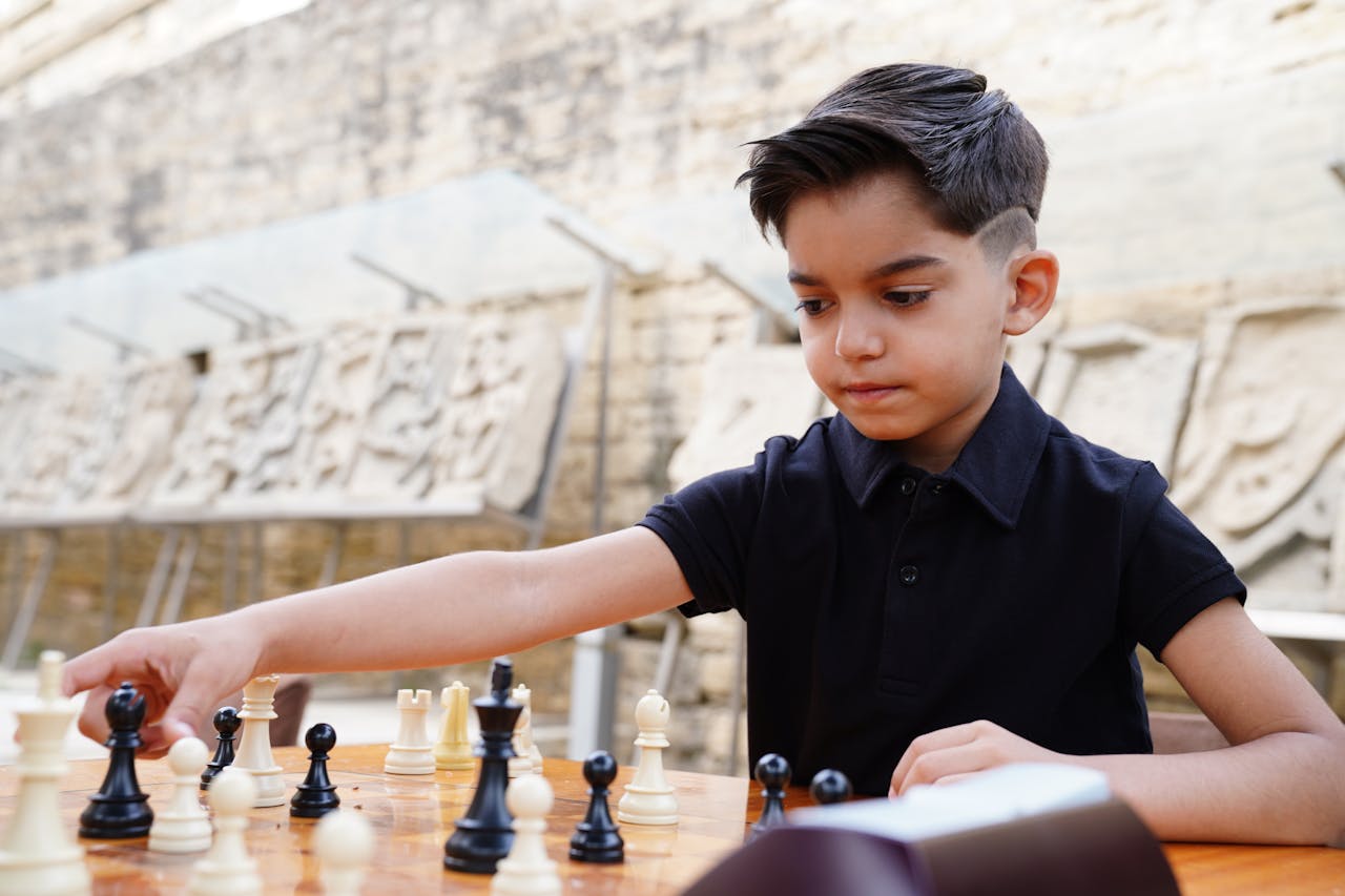 services-03 A young boy focused on a chess game outdoors in a historical stone-carved setting.