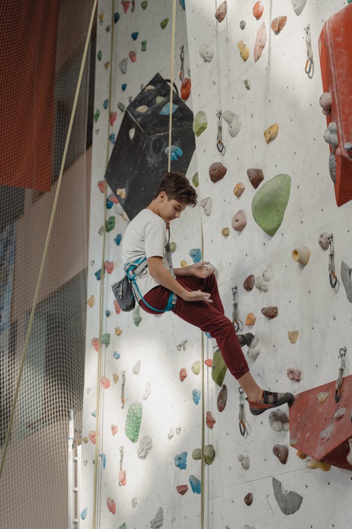 contact-img Young climber practicing indoor wall climbing with safety gear in a gym.