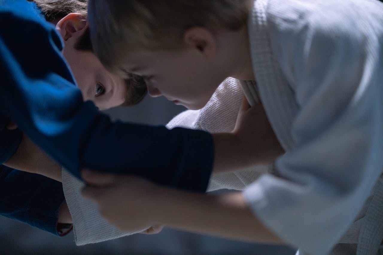 Two young boys engage in jiu jitsu training, focusing on combat skills indoors.