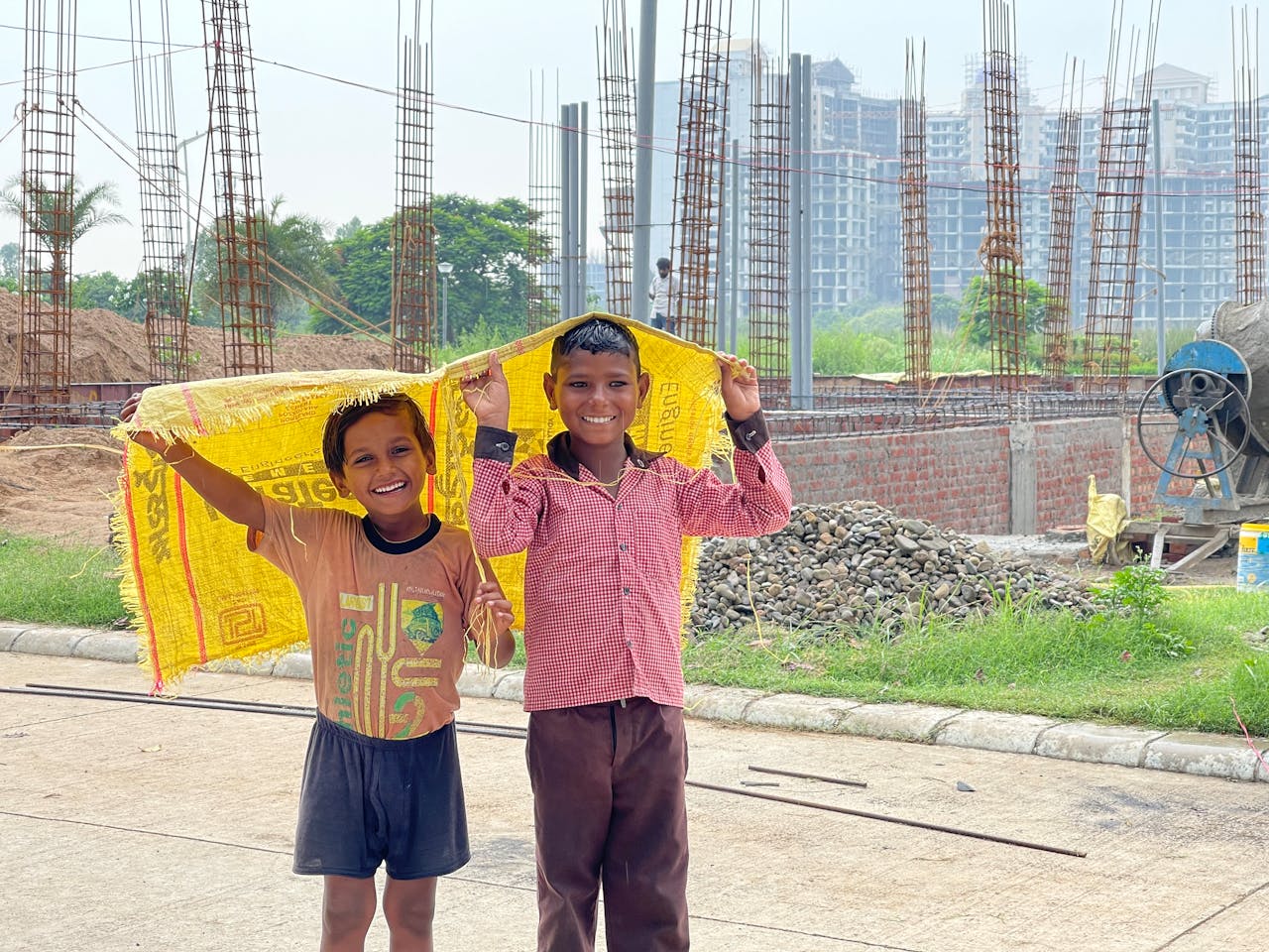 services-02 Two smiling boys holding a yellow sack at a construction site in Rasulpur, Punjab.